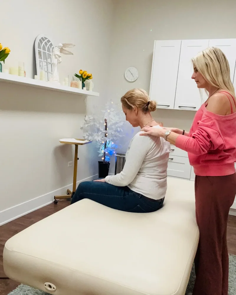 Therapist working on a seated client's shoulders in a treatment room