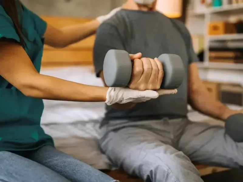 A therapist supporting a seated man's wrist and hand as he holds a dumbbell